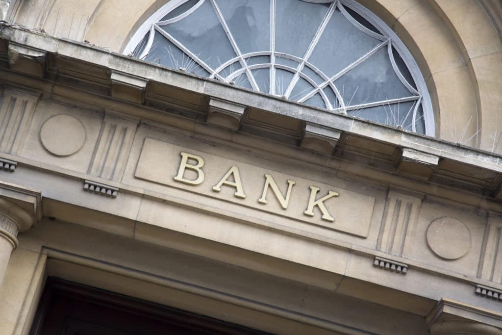 The front of a stone building that says “Bank”, where an accountholder can obtain a Medallion Signature Guarantee.
