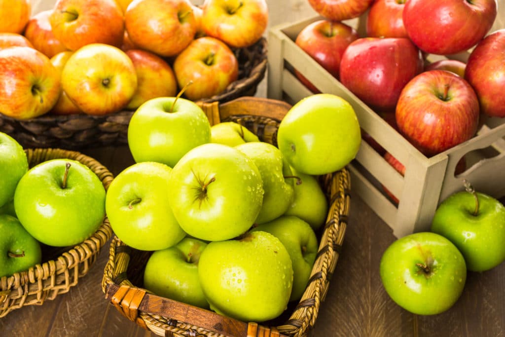 Wicker baskets holding different apples such as Granny Smith, Red Delicious, and Golden Delicious Apples.