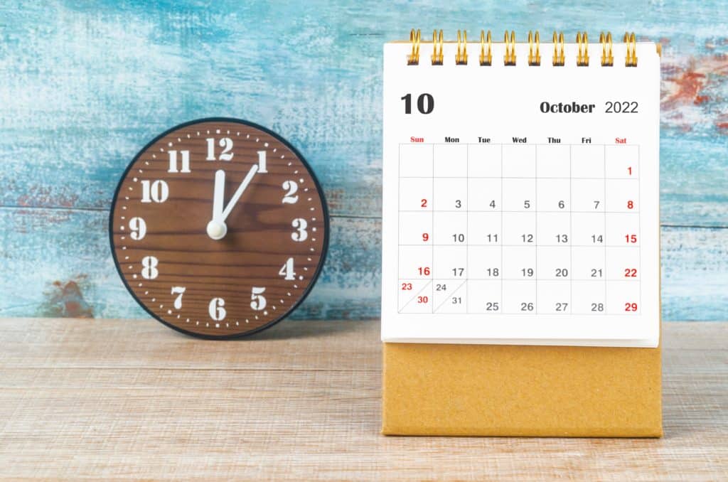October 2022 calendar on a wooden table next to a clock to signify the deadline to correct excess Self-Directed IRA contributions.