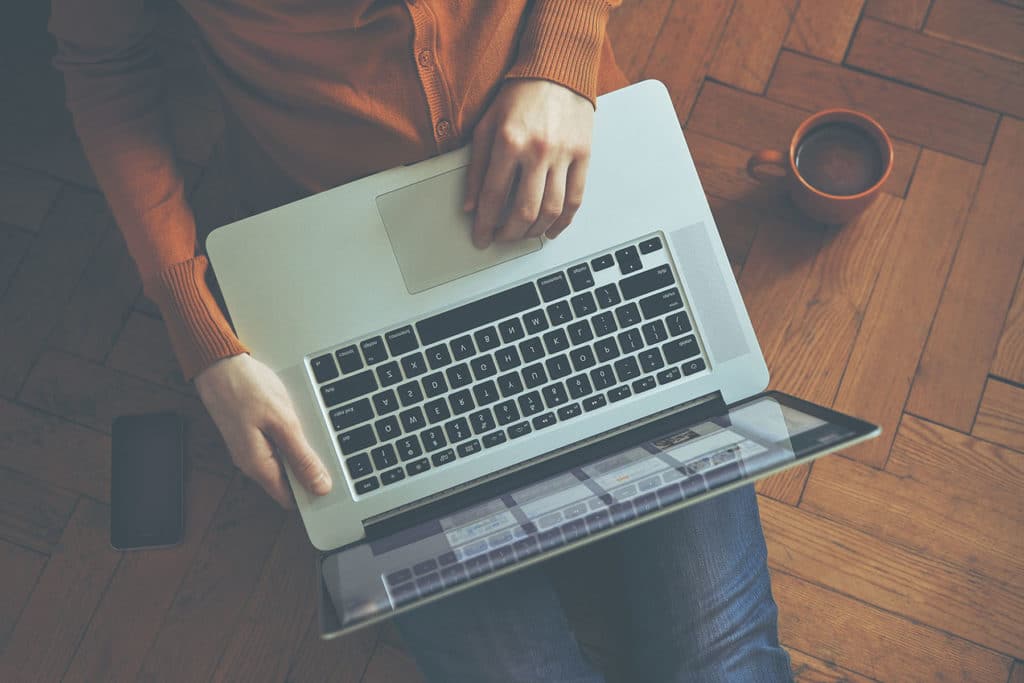 Laptop,in,girl's,hands,sitting,on,a,wooden,floor