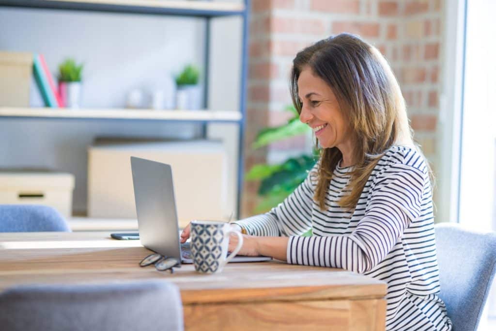 Retired woman smiling while typing on her laptop.